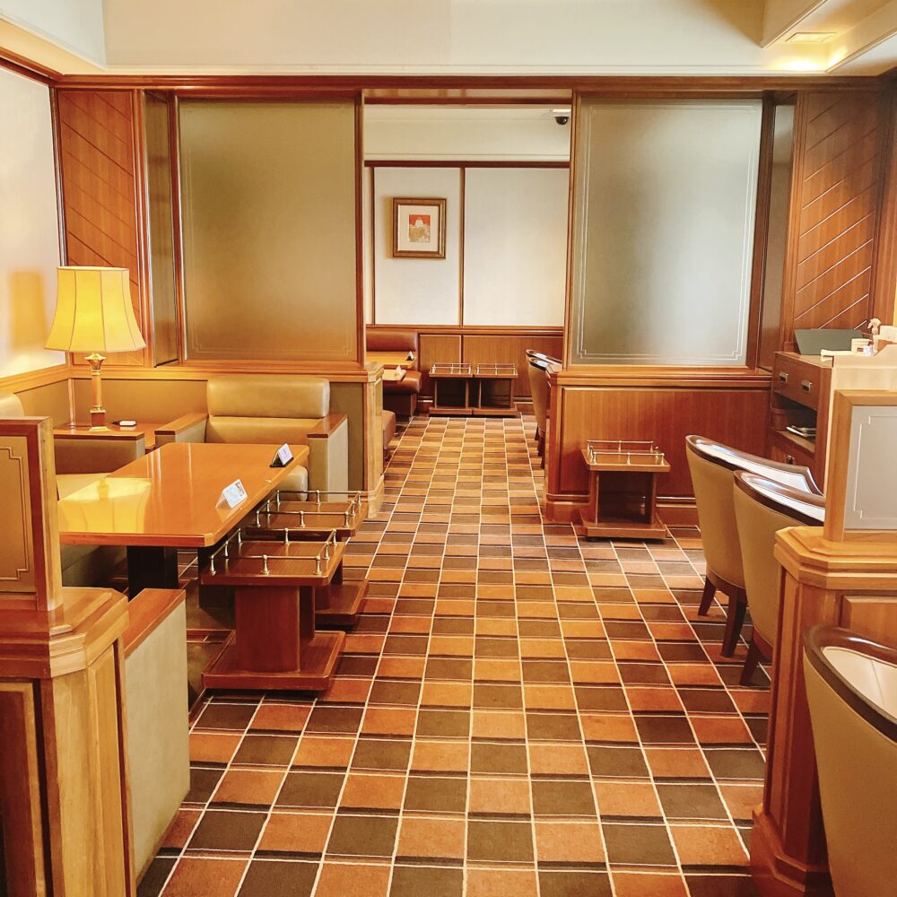 帝国ホテル東京 インペリアルクラブラウンジ内部。木目調の壁と茶色とオレンジのチェック柄のカーペットが特徴的な、重厚で落ち着いた雰囲気の空間。