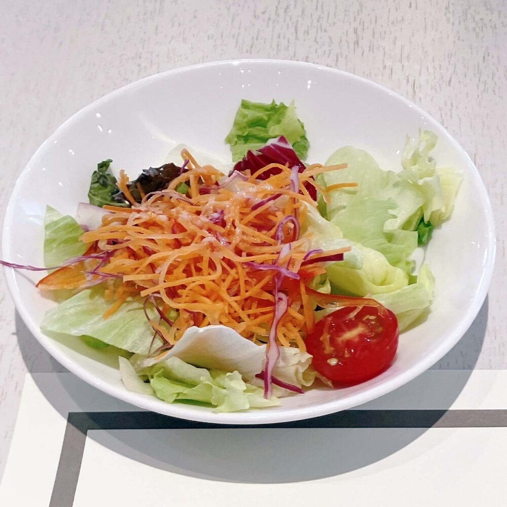帝国ホテル東京パークサイドダイナーで提供された、新鮮な葉物野菜と千切りにんじん、ミニトマトが盛り付けられたサラダ。ドレッシングがかかっている。

