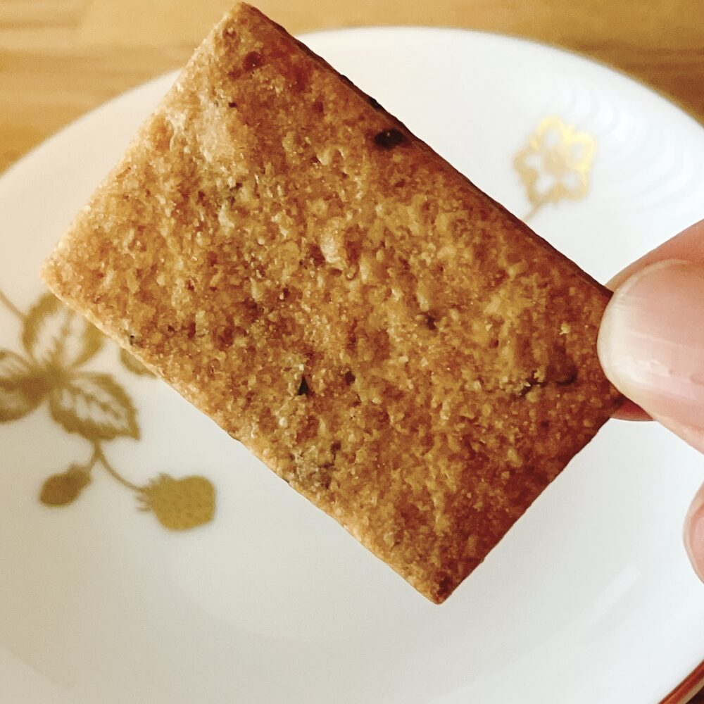 帝国ホテルのプレミアムクッキー缶に入っている、手で持たれた長方形のラムレーズンクッキー。レーズンが練り込まれた生地のサクッとした質感が分かるクローズアップ写真。