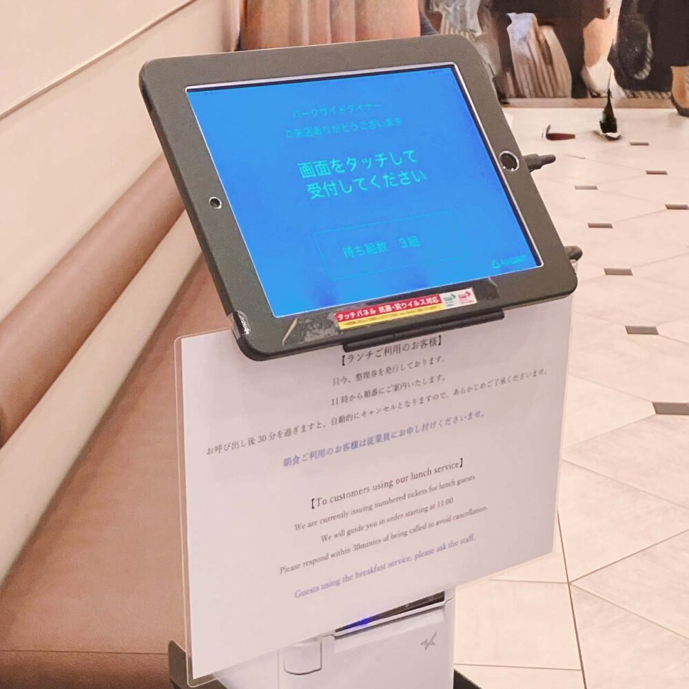 帝国ホテル東京「パークサイドダイナー」の入り口に設置されたタブレット型の順番待ち受付機。画面には「画面をタッチして受付してください」と日本語で表示され、その下にはランチ利用の案内文が書かれている。