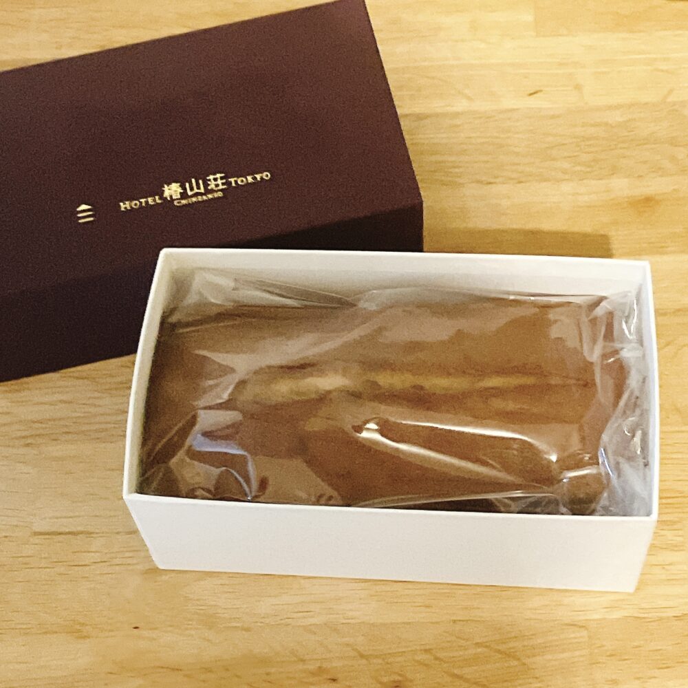 ホテル椿山荘東京の栗のパウンドケーキが、濃いワインレッド色の箱から取り出され、白い内箱に収まった状態。パウンドケーキはビニールで密封されている。