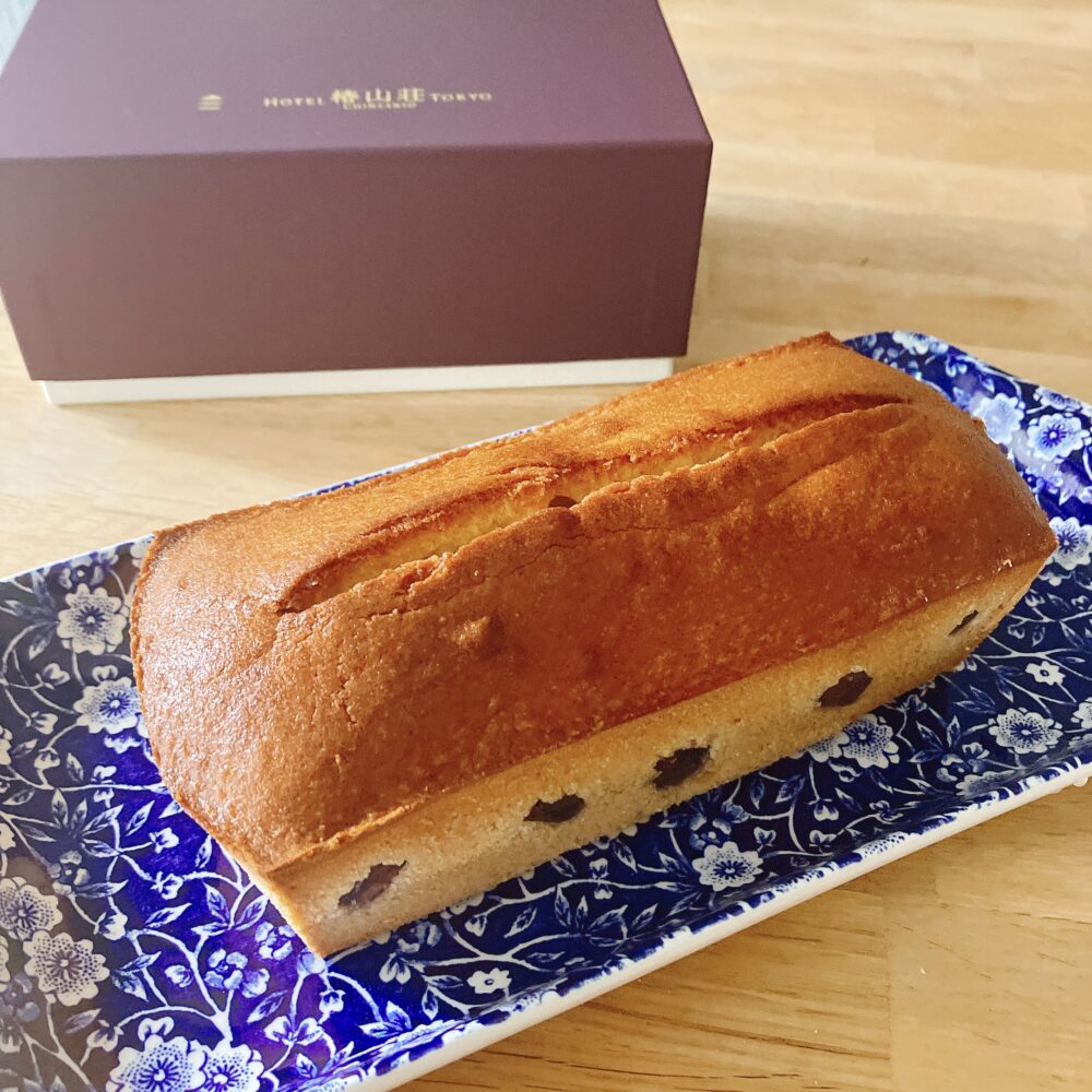 ホテル椿山荘東京の栗のパウンドケーキ全体像。焼き色のついた生地の側面に、大きな栗がいくつか覗いているのが確認できる。奥にはホテルのロゴが入ったワインレッドの箱が置かれている。