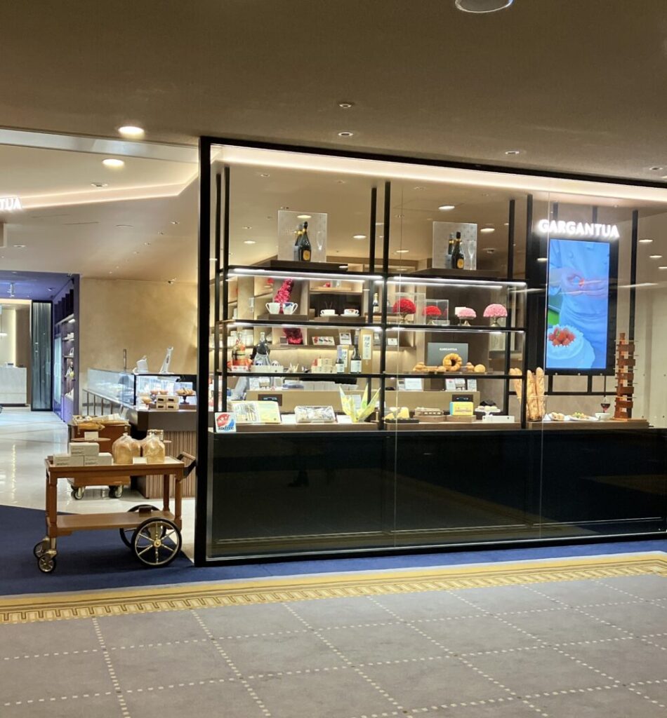 帝国ホテル東京本館地下1階にあるホテルショップ「ガルガンチュワ」の外観。ガラスのショーケースにパンやスイーツが並び、手前には木製のカートにパンが積まれている。