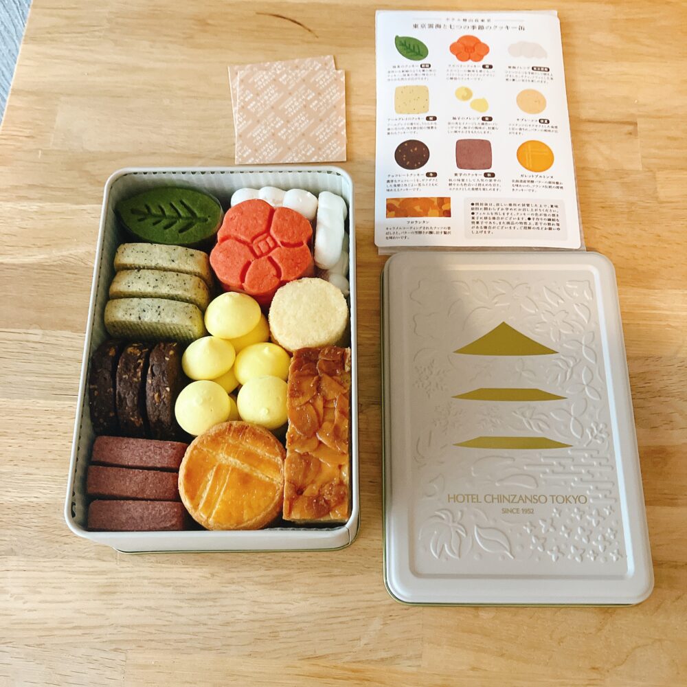 ホテル椿山荘東京「東京雲海と七つの季節のクッキー缶」の開封写真。白い缶の横に、全10種のクッキーがぎっしり詰まった中身と解説カードが並んでいる。