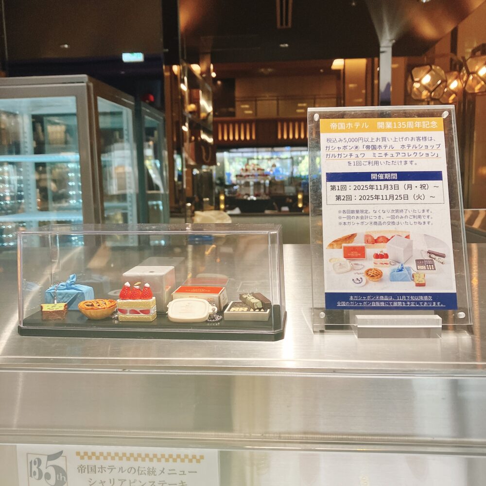 帝国ホテル ガルガンチュワの「開業135周年記念ガチャポン」。5,000円以上購入で利用可能なキャンペーンで、ミニチュアケーキの景品サンプルが展示されている。