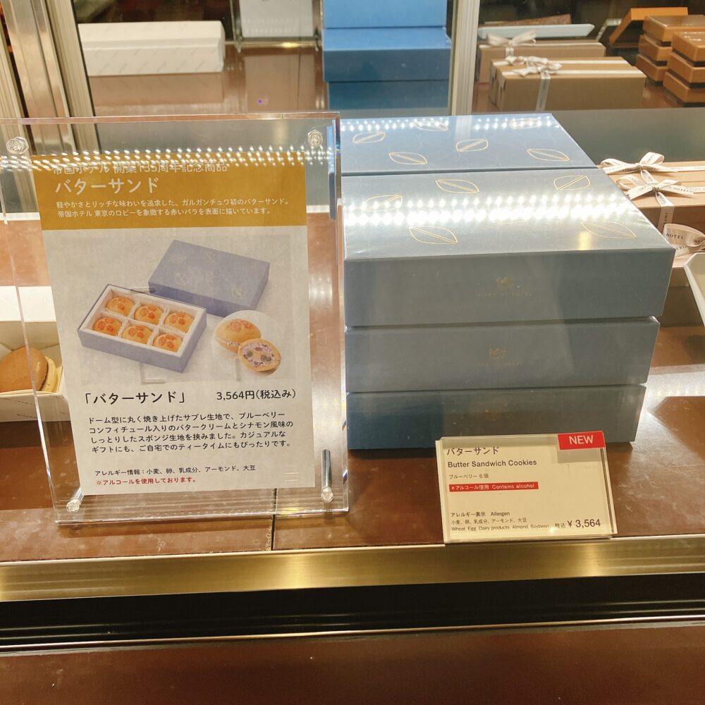 帝国ホテル ガルガンチュワのショーケースに並ぶ、開業135周年記念の新作「バターサンド」。青いパッケージが数段積み重ねられており、商品の説明ボードが添えられている。