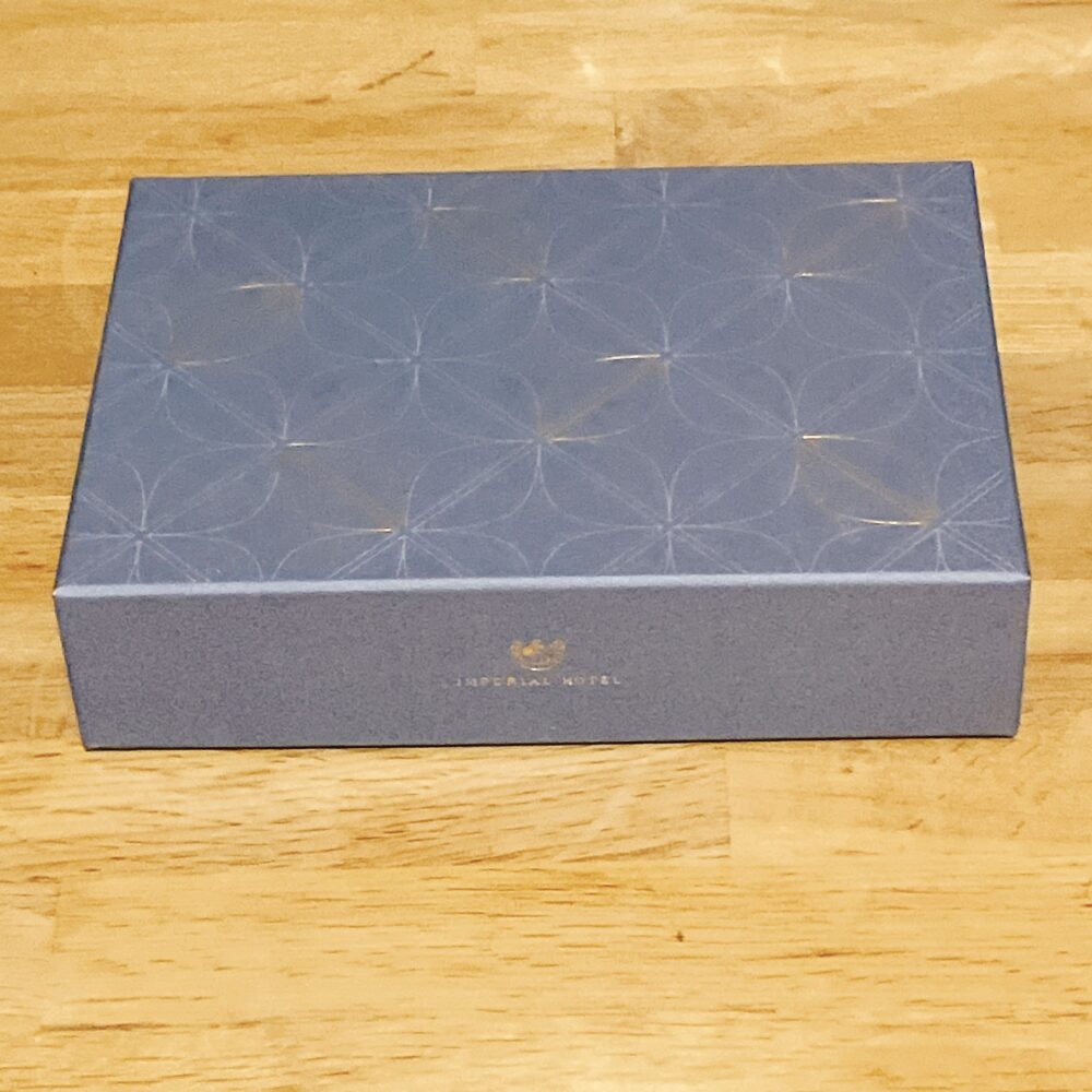 帝国ホテル 135周年記念のバターサンドのパッケージ。濃いブルーの箱で、蓋の中央には金色の帝国ホテルのロゴ（クラウン）がデザインされている。