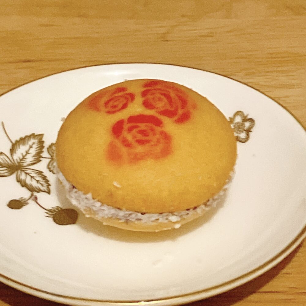 帝国ホテル 135周年記念のバターサンドのクローズアップ写真。ドーム型サブレの上には赤いバラの模様が描かれ、周囲にはココナッツパウダーがまぶされているのが見える。