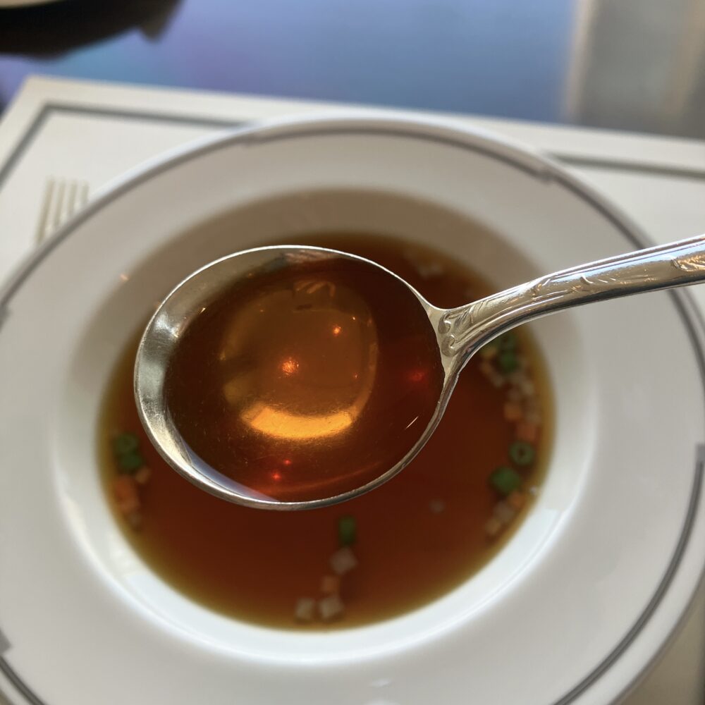 帝国ホテルのダブルビーフコンソメ。スプーンに掬われたスープが琥珀色に輝き、高い透明度と濃厚な質感が強調されている。