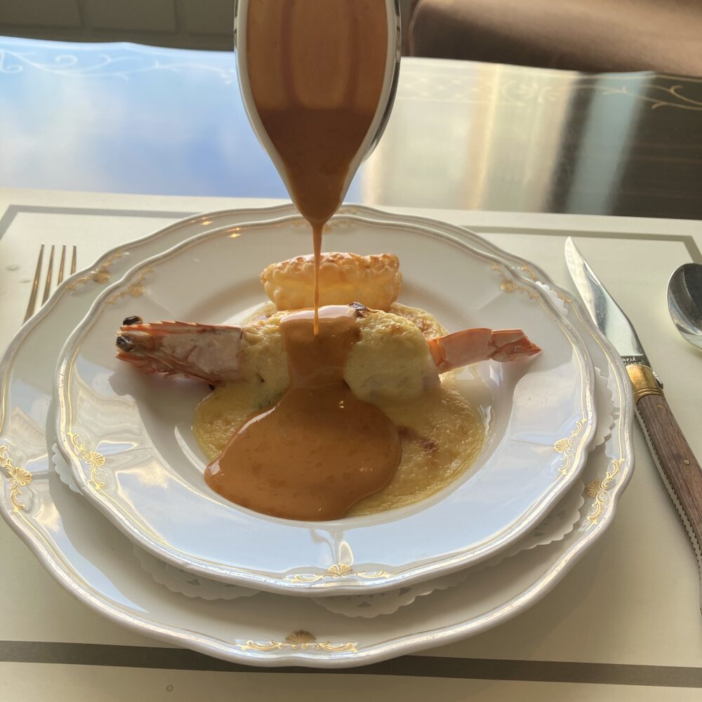 ホテルマンがソースポットから、舌平目と車海老のグラタン「レーヌ・エリザベス」にソースを注ぐサービスシーン。