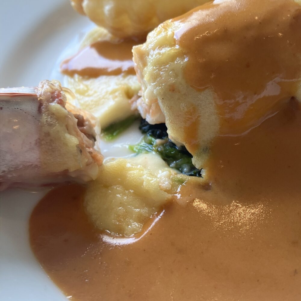 舌平目のグラタンの断面。中には大きな車海老とソテーされたほうれん草が詰まっており、海老のソースがたっぷりとかかっている。