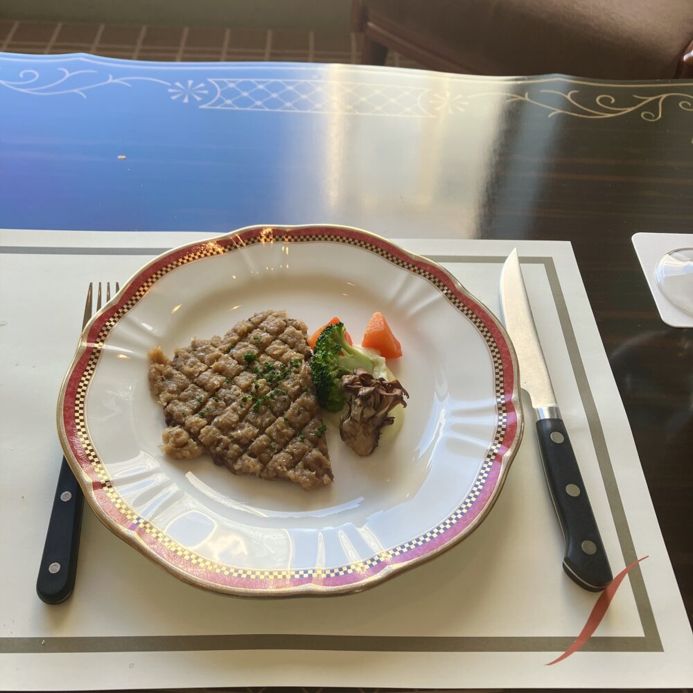 帝国ホテルのシャリアピンステーキ。格子状の焼き目がついた肉の上に炒めた玉ねぎが敷き詰められ、ブロッコリーと人参、舞茸が添えられている。