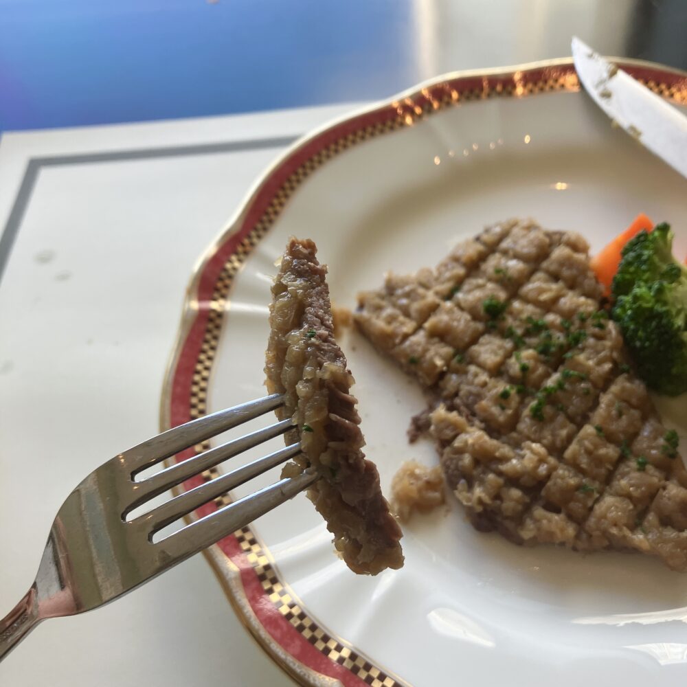 フォークで持ち上げられたシャリアピンステーキの断面。肉の上に玉ねぎが層になって乗っている様子。