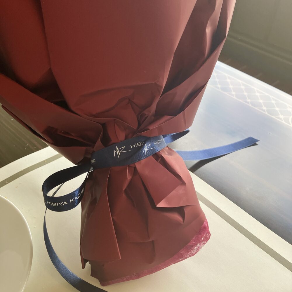 日比谷花壇のロゴ（HIBIYA KADAN）が入った紺色のリボンで結ばれた、深紅の花束のラッピングのアップ。
