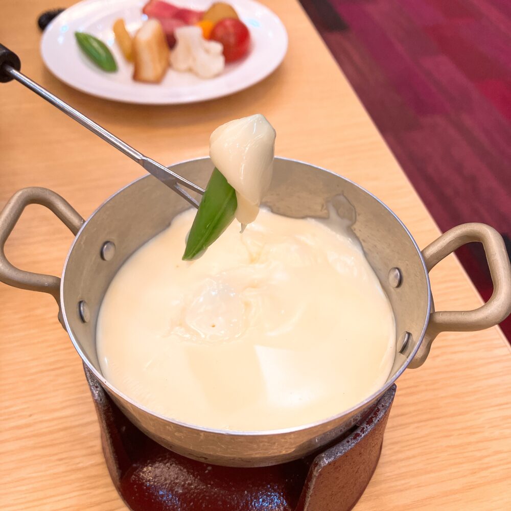 スナップエンドウをとろとろの熱々チーズフォンデュにディップしている様子。