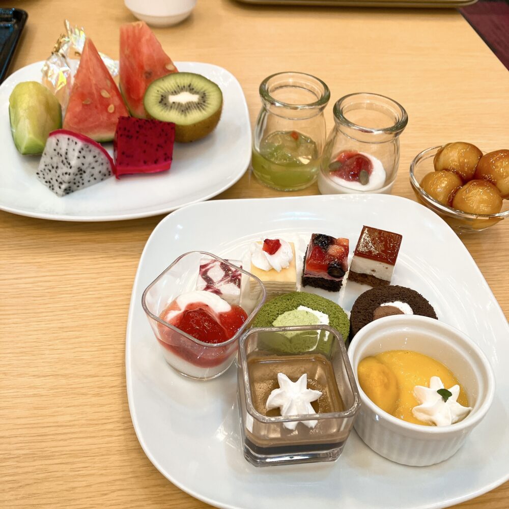 スイカやドラゴンフルーツなどのフルーツと、色とりどりな一口サイズのケーキを盛り付けた豪華なデザートプレート。右奥にはみたらし団子も。