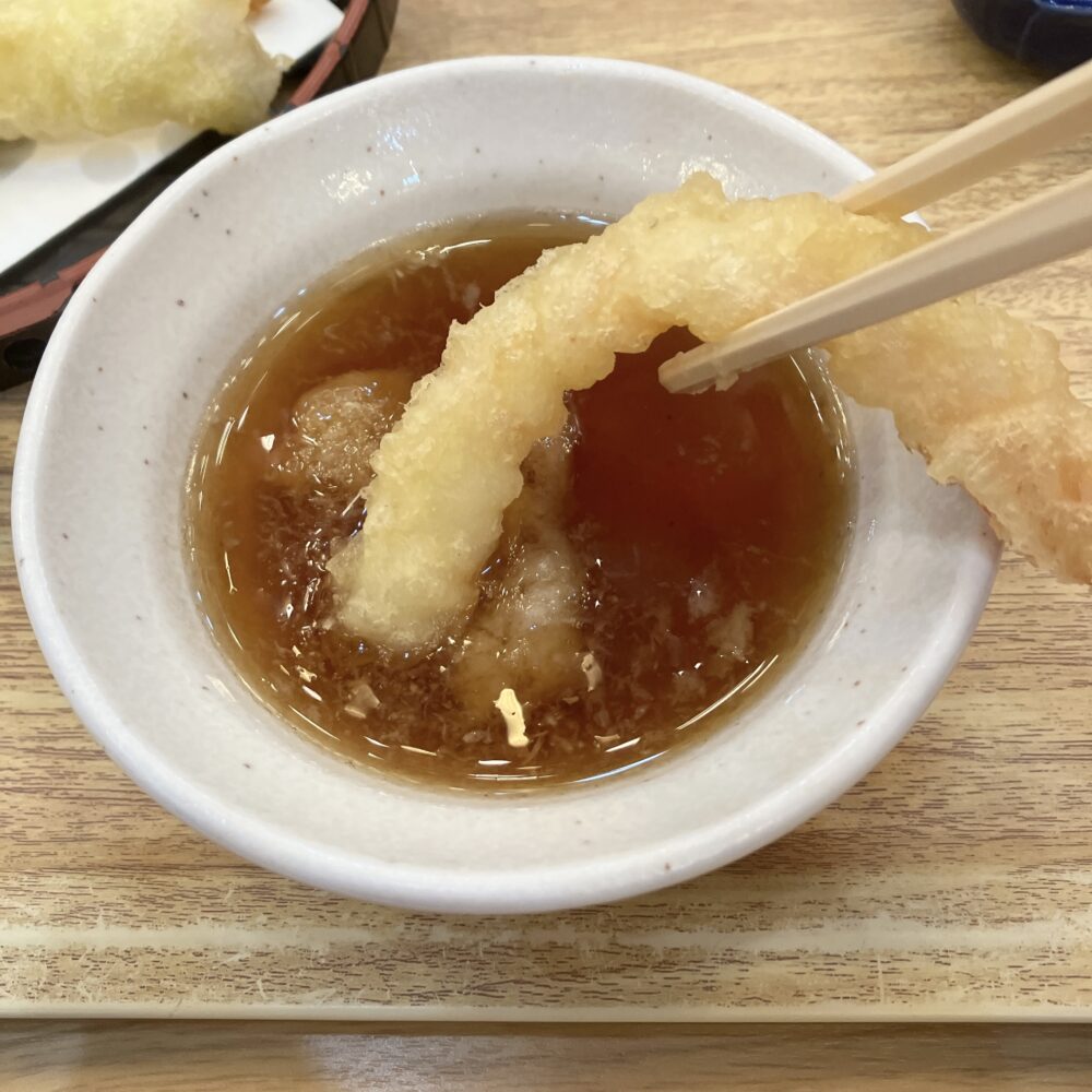揚げたての海老天ぷらを、大根おろしがたっぷり入った天つゆにくぐらせている様子