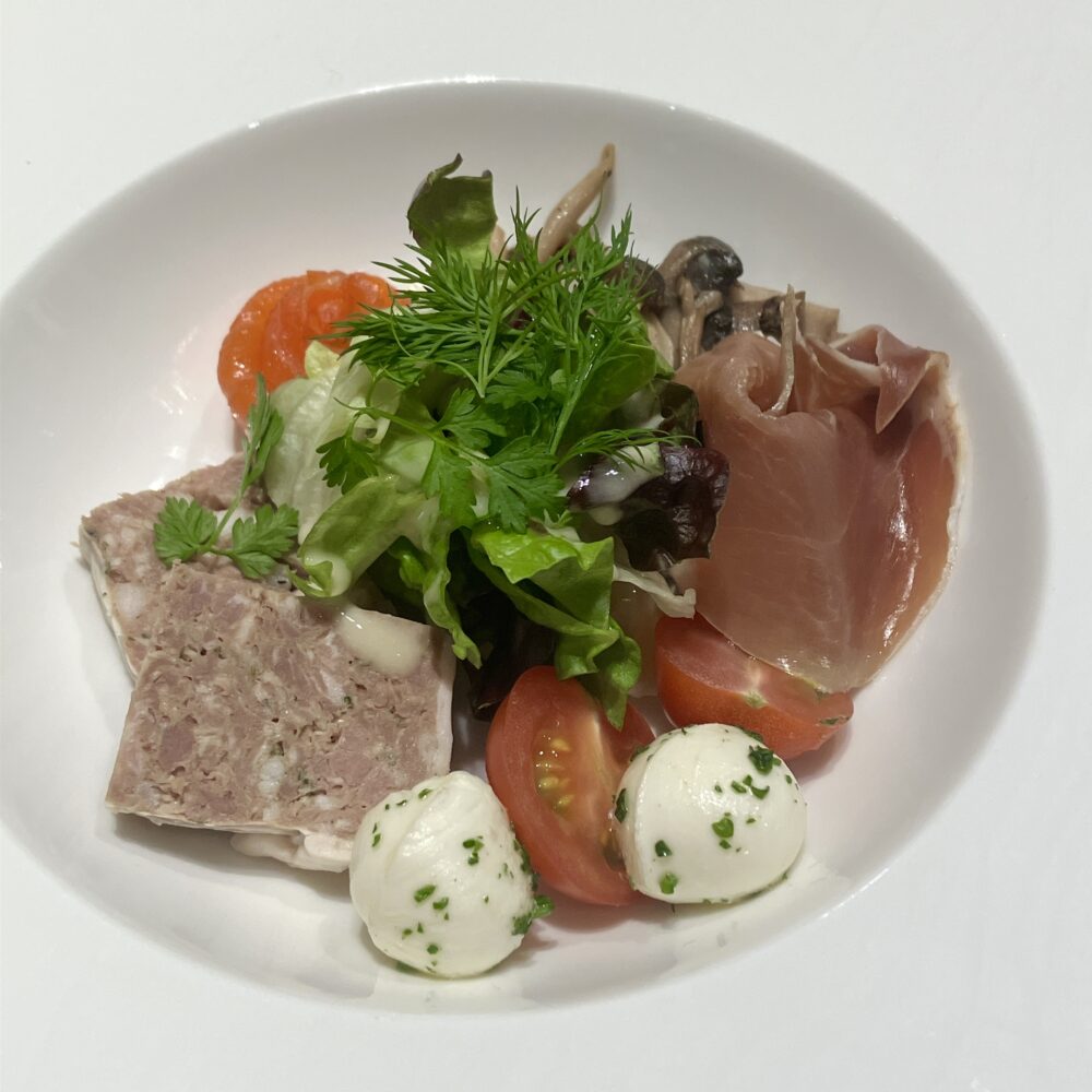 日本橋高島屋特別食堂の前菜「美食家のサラダ」。サーモンのバラ飾り、パテ・ド・カンパーニュ、生ハム、モッツァレラチーズなどの高級食材が、グリーンサラダを囲むように盛り付けられた一皿。