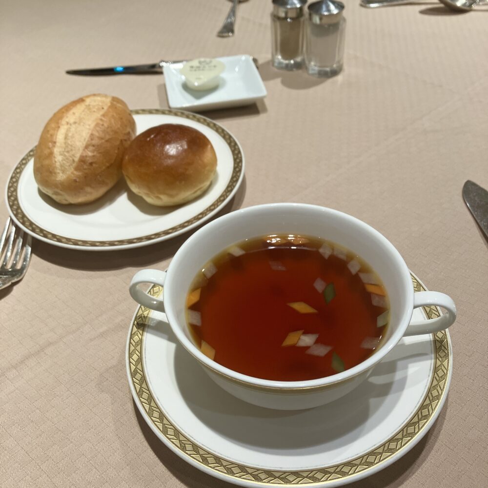 美しい琥珀色に澄んだダブルビーフコンソメスープのカップと、その横に添えられた温かいロールパンとブリオッシュ。夏バテした体に染み渡った、私にとっての「命のスープ」。
