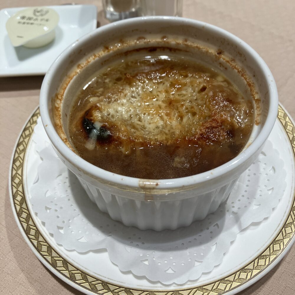 帝国ホテル伝統のオニオングラタンスープ。たっぷりのグリュイエールチーズがこんがりと狐色に焦げ目がつき、熱々の状態でココット皿に入れられている。母が「人生で一番美味しい」と絶賛した濃厚なスープ。