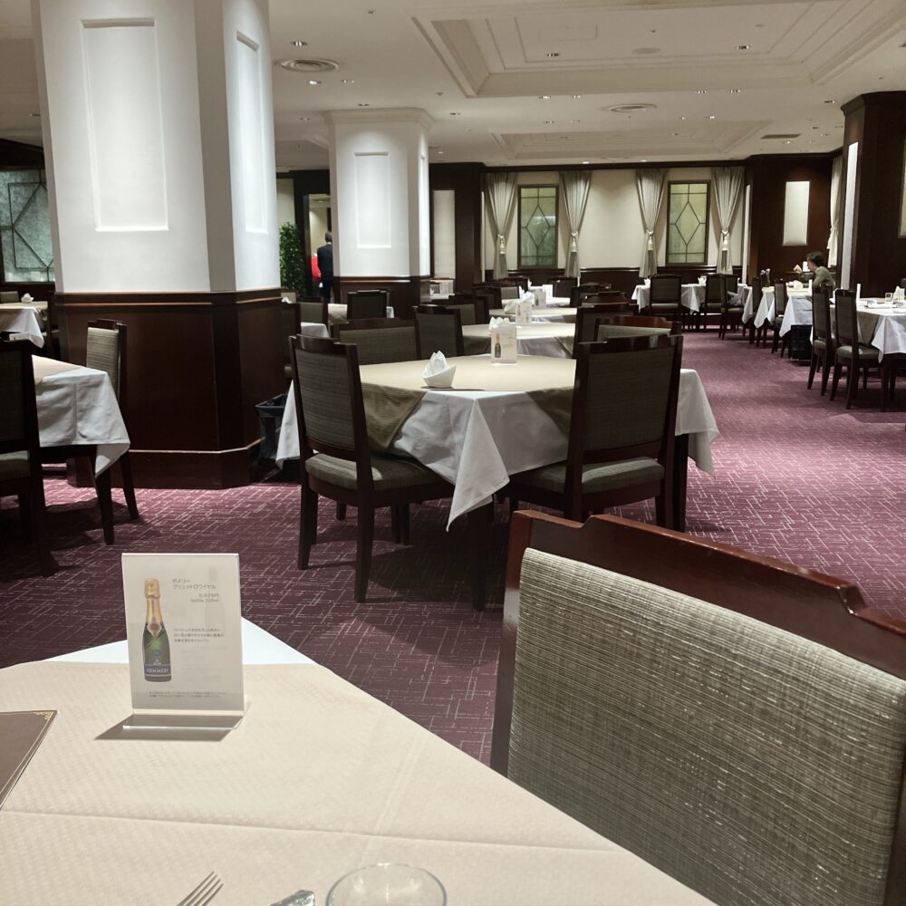 日本橋高島屋特別食堂の広々とした店内。赤い絨毯が敷き詰められ、太い白い柱が天井を支えている。白いクロスが掛かったテーブルは間隔を広く取って配置されており、格式高いホテルのメインダイニングのような雰囲気。