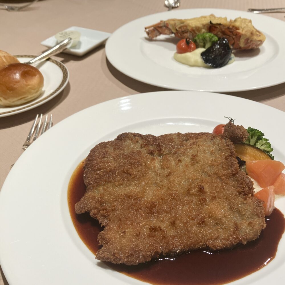 日本橋高島屋特別食堂のメインディッシュ。手前には皿からはみ出しそうな巨大な仔牛のカツレツ、奥には上品な伊勢海老のテルミドールが並び、そのボリュームの差が際立っている。