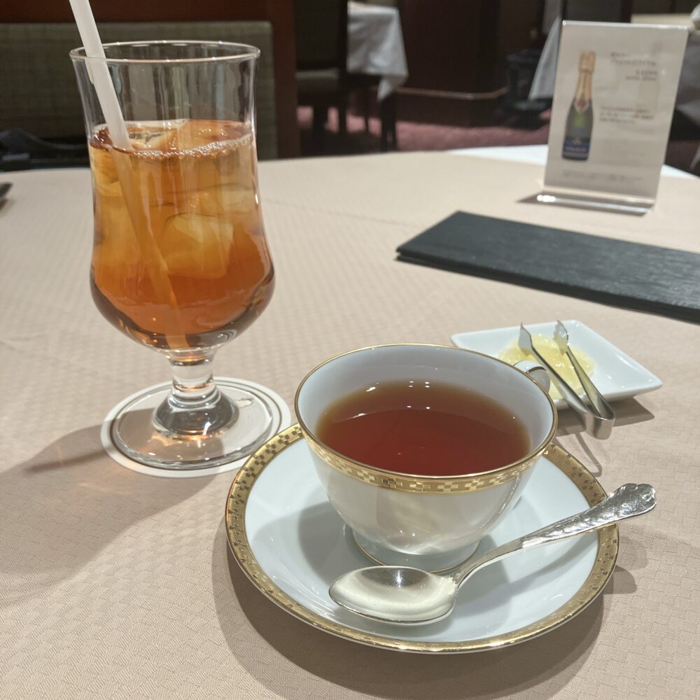 食後のホットティーとアイスティー。帝国ホテルの紋章が入った金縁のティーカップと、涼しげなアイスティーのグラスが並び、レモンスライスが添えられている。おかわり自由で提供される。