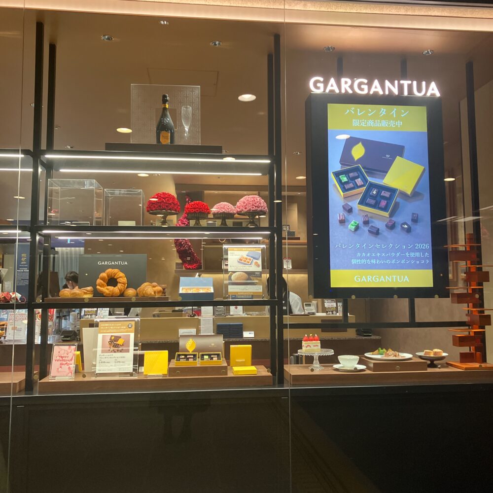 帝国ホテル「ガルガンチュワ」のショーウィンドウ。デジタルサイネージには「バレンタイン限定商品販売中」と表示され、市川シェフの新作ショコラのポスターと商品がディスプレイされている。