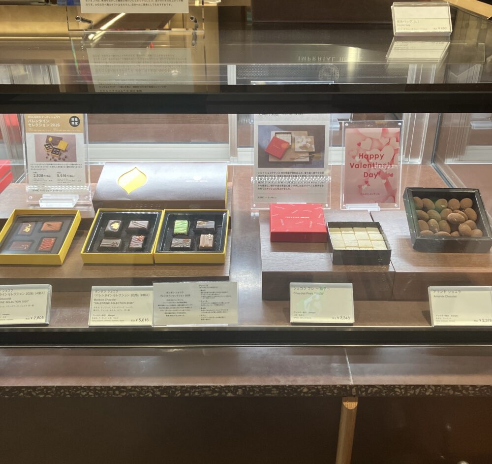 店内のショーケースに並ぶバレンタイン限定ショコラ。左側には新作の「ボンボン ショコラ バレンタインセレクション 2026（4個入・8個入）」、右側には赤い箱に入った店頭限定の「ショコラ フレ ～柚子～」と「アマンド ショコラ」が陳列されている。