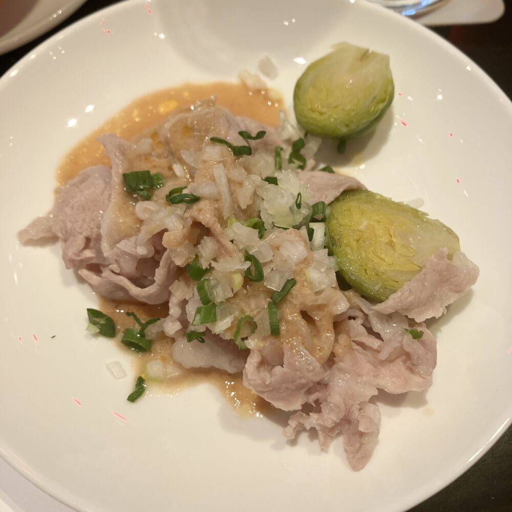 茹でた薄切りの豚肉に、胡麻ソースとネギがたっぷりかかった松坂豚の胡麻ソース。芽キャベツが添えられている。