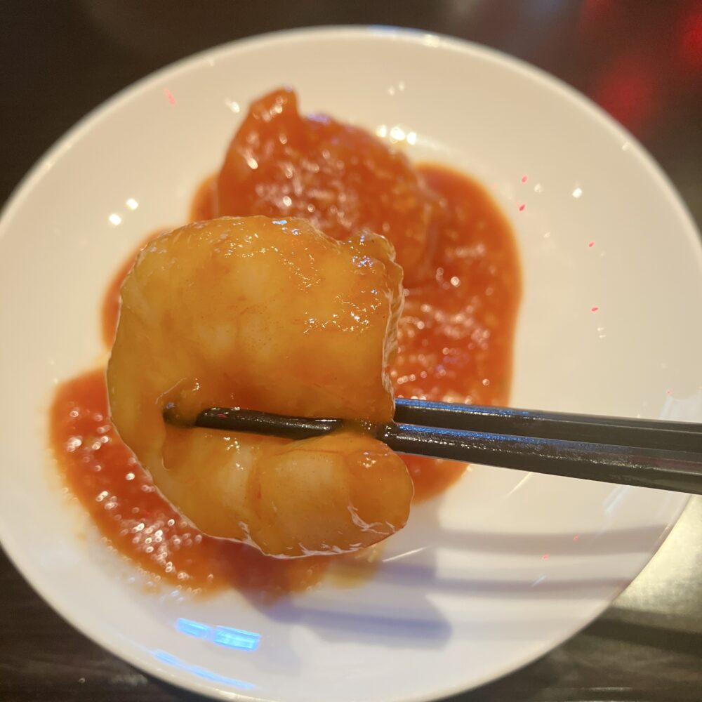 箸で持ち上げられた、大ぶりでツヤのあるチャイナルームの海老のチリソース炒め。