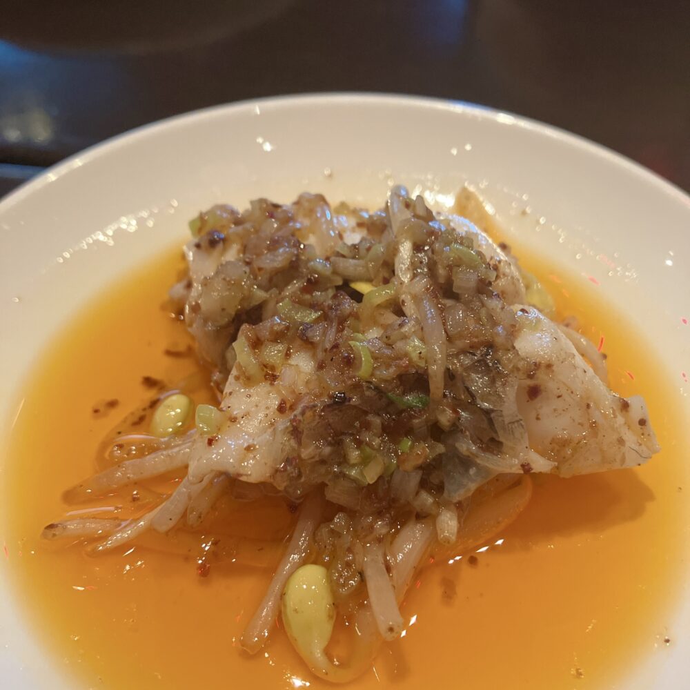 真鯛のチリオイルがけ」。薬味がたっぷり乗ったふっくらとした白身魚に、鮮やかなオレンジ色のチリオイルが絡んでいる