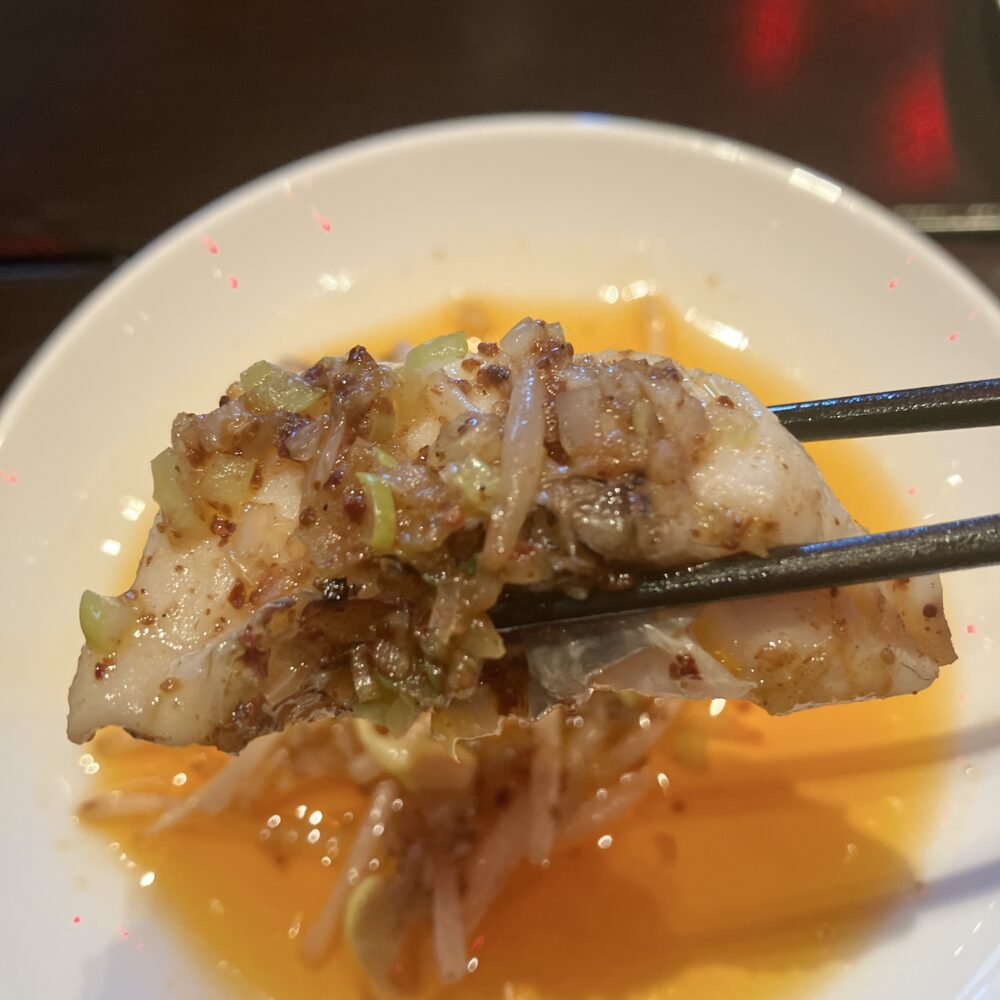 箸で持ち上げられた「真鯛のチリオイルがけ」。薬味がたっぷり乗ったふっくらとした白身魚に、鮮やかなオレンジ色のチリオイルが絡んでいる｜チャイナルーム