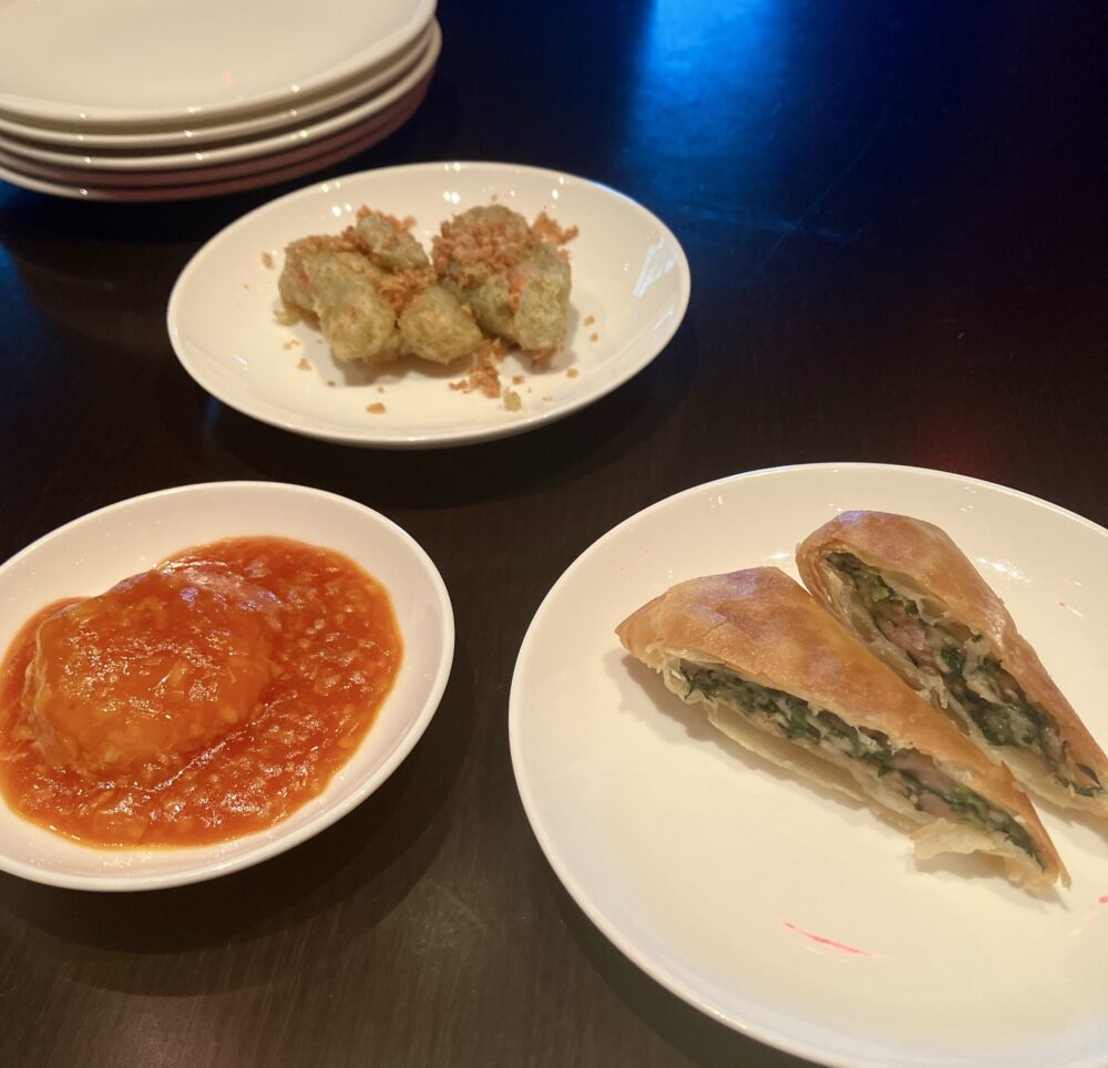 テーブルに並んだ3種類のお皿。エビチリ、ズワイ蟹のフライドガーリック、そして断面から緑色の春菊が見える春巻き。