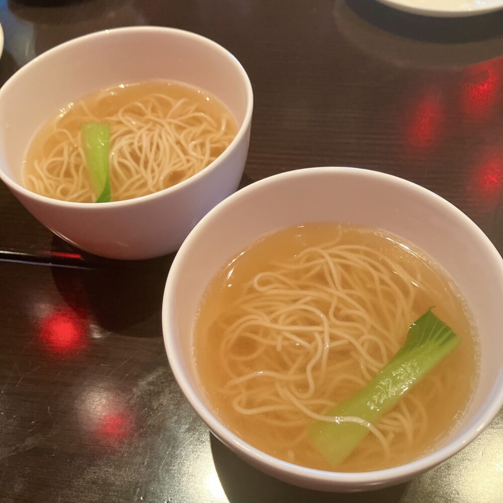 小さめの器で提供された、チャイナルームの金華ハムの香り 醤油汁そば。透き通ったスープに細麺と青梗菜が入っている。