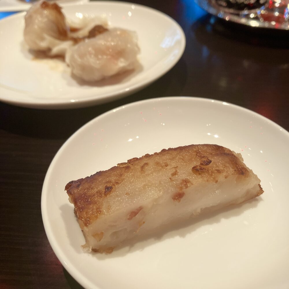 手前の白い皿に、表面がきつね色にこんがりと焼かれた厚切りの大根餅。奥の皿には蒸し点心（エビ蒸し餃子など）が並んでいる、チャイナルームでの飲茶の様子。