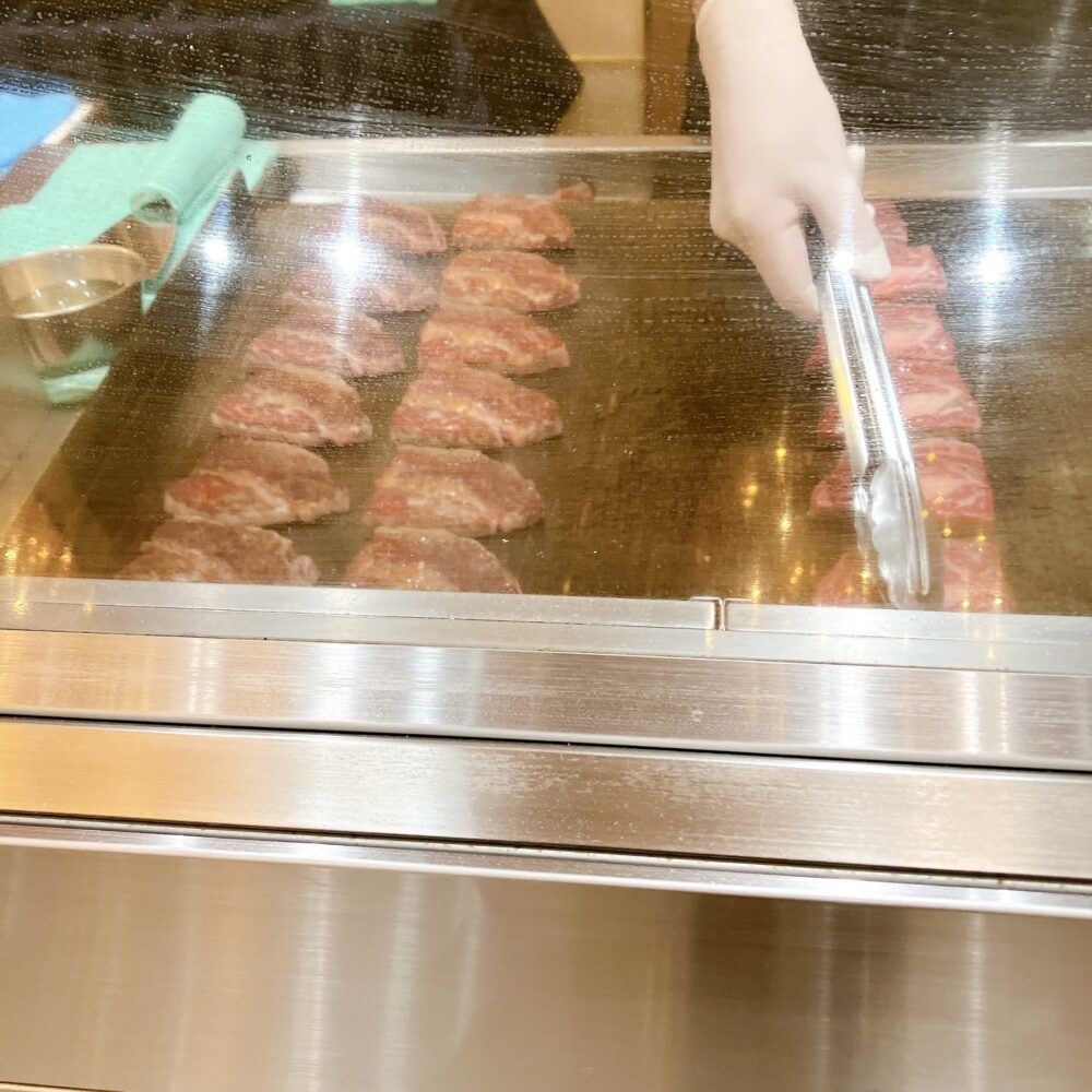 ライブキッチンの鉄板で、ステーキ肉がジューッと音を立てて焼かれている様子