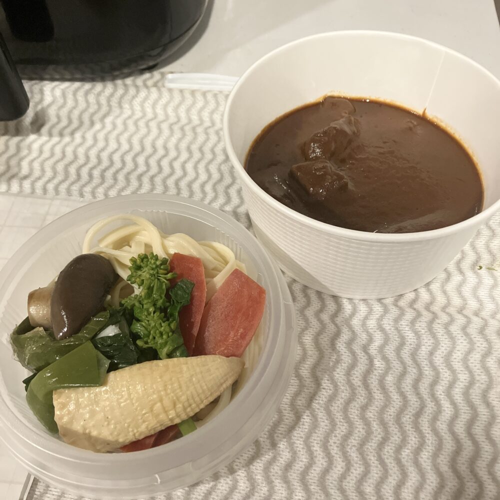 テイクアウト用の容器に入ったビーフシチュー。ソースと牛肉が入った容器と、ヌードルと色鮮やかな京野菜（筍、菜の花、人参など）が入った容器が別々に分けられている。