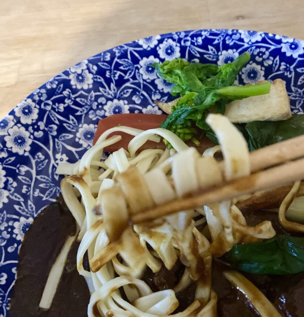 箸で持ち上げられた平打ちのヌードル。帝国ホテルのドミグラスソースがしっかりと絡んでいる。