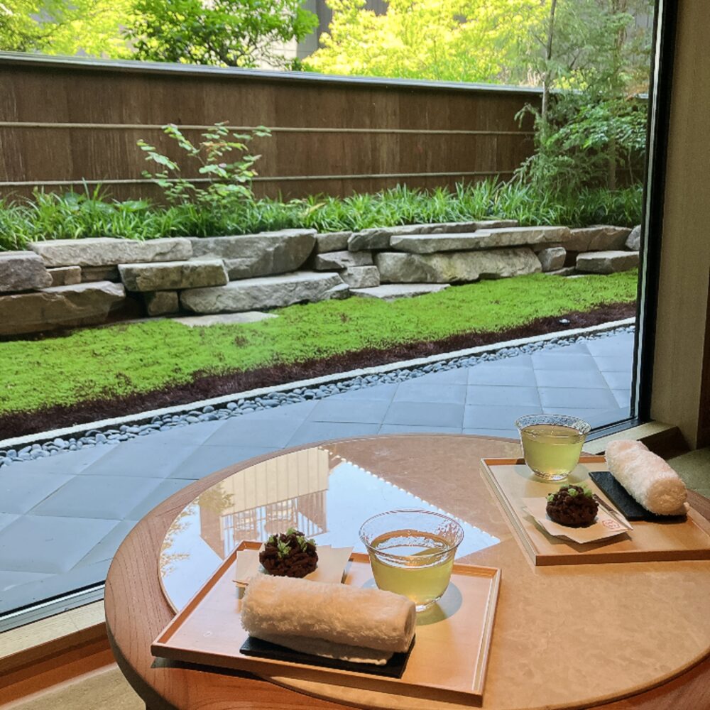 帝国ホテル京都のチェックイン時に提供されるウェルカムドリンクと和菓子。窓越しの美しい緑を背景に