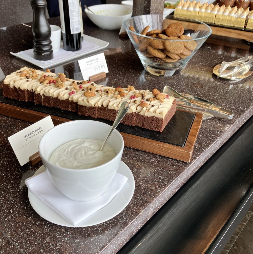 ニューヨークグリルのスイーツブッフェ台。クリームやナッツが美しくトッピングされたチョコレートケーキ、添えられたフロマージュブラン、そして奥にはガラスボウルに入ったチョコレートチップクッキーが並んでいる。