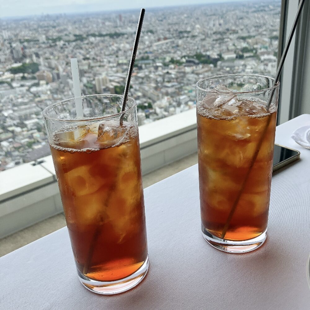 パークハイアット東京 ニューヨークグリル41階の窓際テーブルに並ぶアイスティー2杯。琥珀色の液体が透明なグラスに満たされ、眼下に広がる東京の街並みを背景に清涼感あふれる一枚。