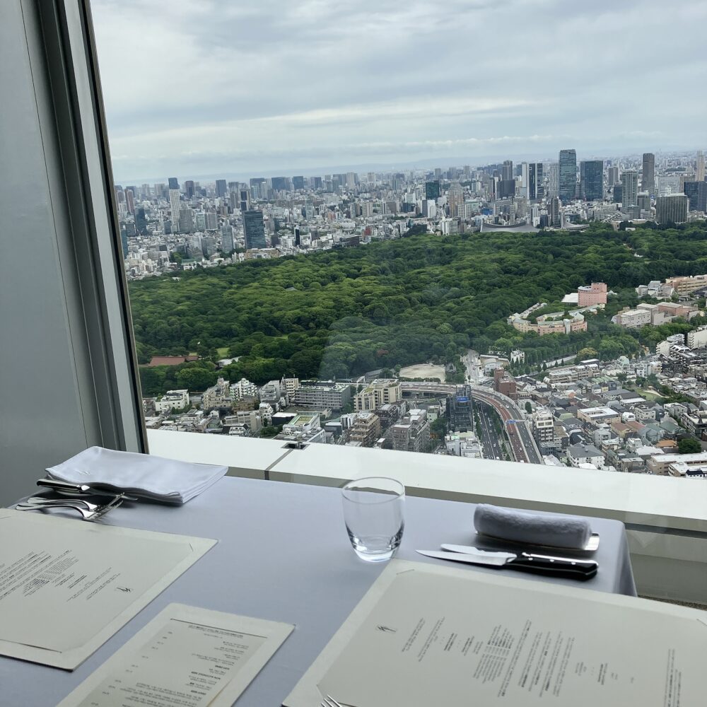 パークハイアット東京 ニューヨークグリル41階の窓際席。眼下に代々木公園の深い緑が広がり、新宿の高層ビル群が連なる東京の絶景を望む特等席のテーブルセッティング。