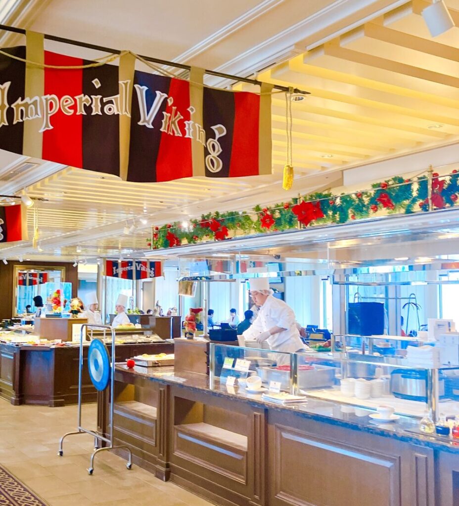 帝国ホテル「インペリアルバイキング サール」のクラシカルな店内。「Imperial Viking」の伝統的なフラッグが飾られ、開放的なテーブル席と活気あるビュッフェカウンターが広がっている様子。