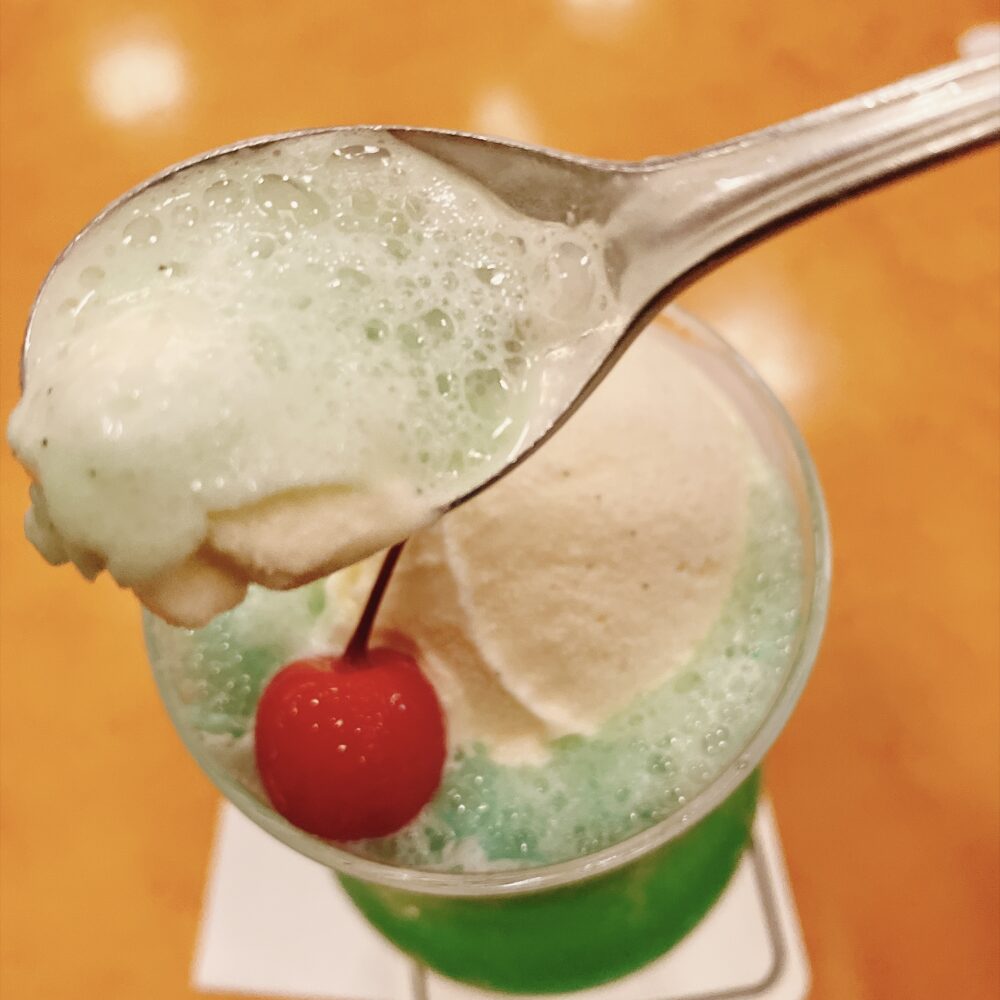 メロンソーダの上のバニラアイスをスプーンですくった様子。ソーダと混ざって氷結し泡立った部分が美味しそうに写っている。