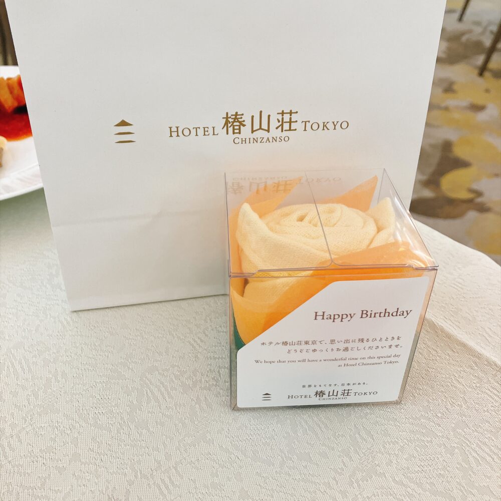 テーブルにさりげなく置かれていた椿山荘からの誕生日サプライズ特典。「Happy Birthday」と書かれたクリアボックス入りのオレンジ色の薔薇の形をしたタオルギフト
