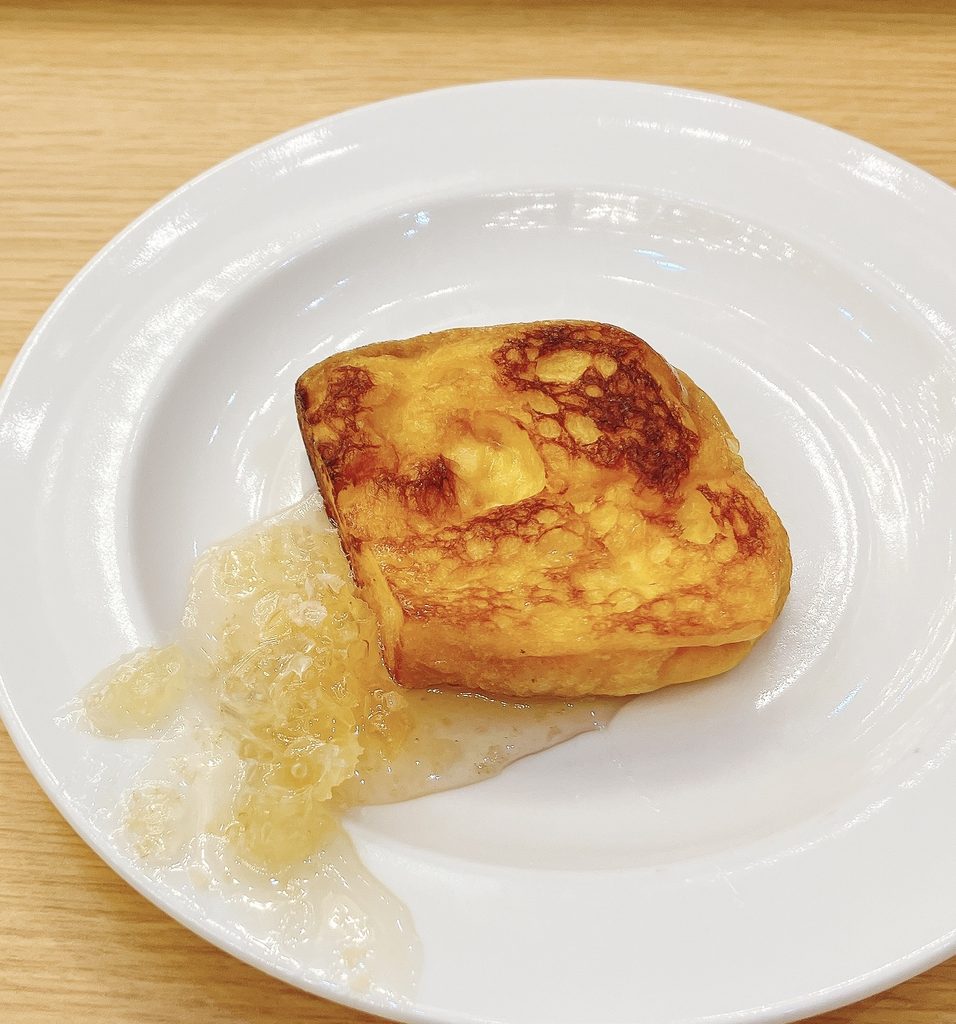 白いお皿に乗った、こんがりと焼き上げられたフレンチトースト。横には巣蜜（はちみつ）が添えられている。