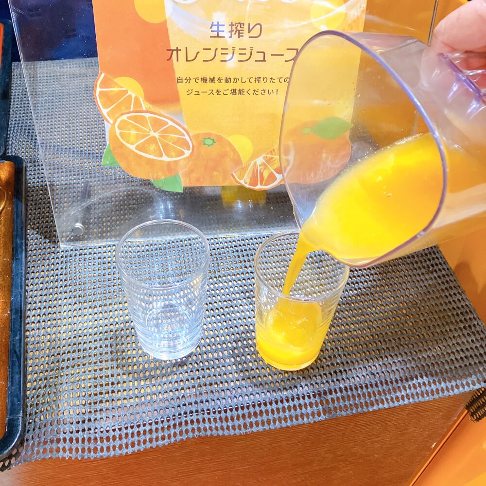ピッチャーからグラスに注がれる、鮮やかな黄色の搾りたてオレンジジュース。