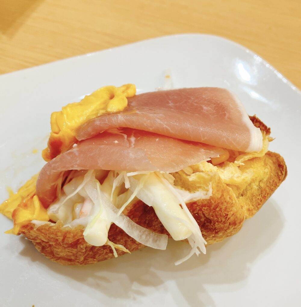 白いお皿に乗せられた、外側がこんがり焼き上がったポップオーバーに生ハム、スクランブルエッグ、マカロニサラダを乗せたもの。