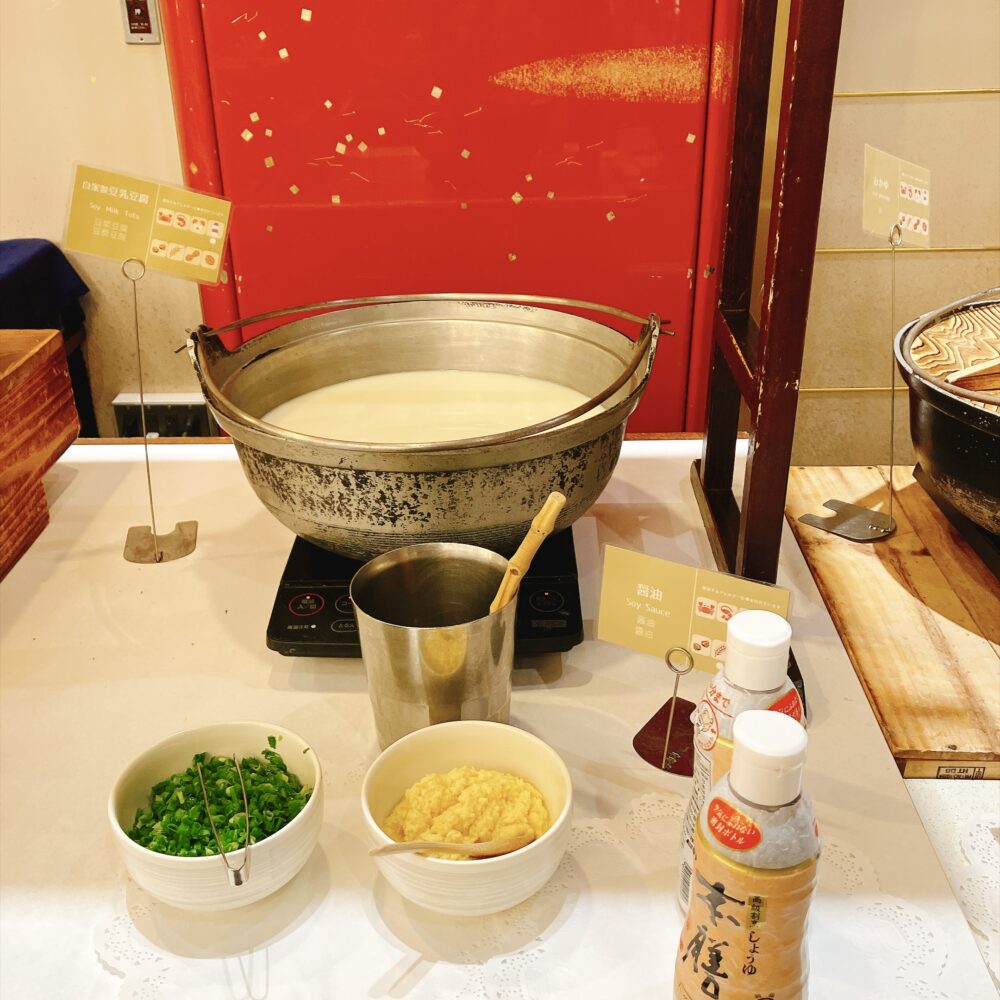 大きな鍋に入った自家製豆乳豆腐。ネギや生姜などの薬味と醤油が手前に用意されている。